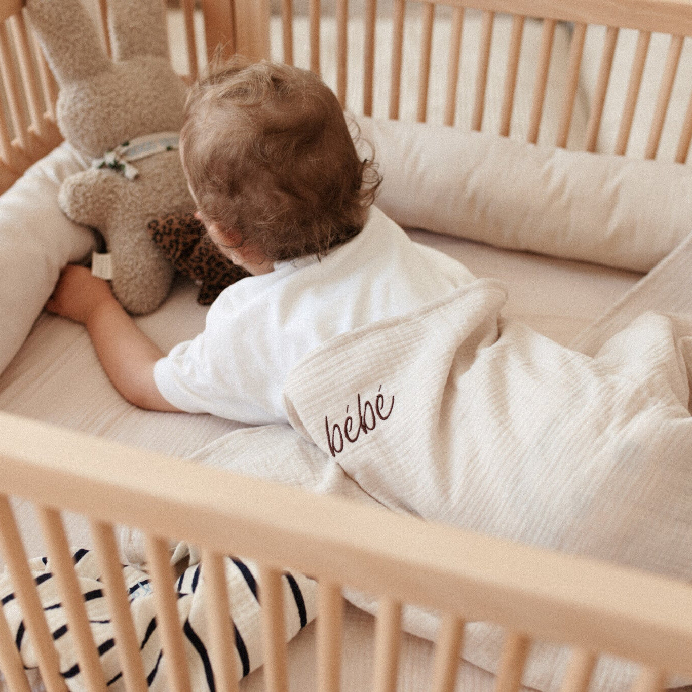 baby ligt onder laken met gepersonaliseerde tekst en houdt een knuffel vast.