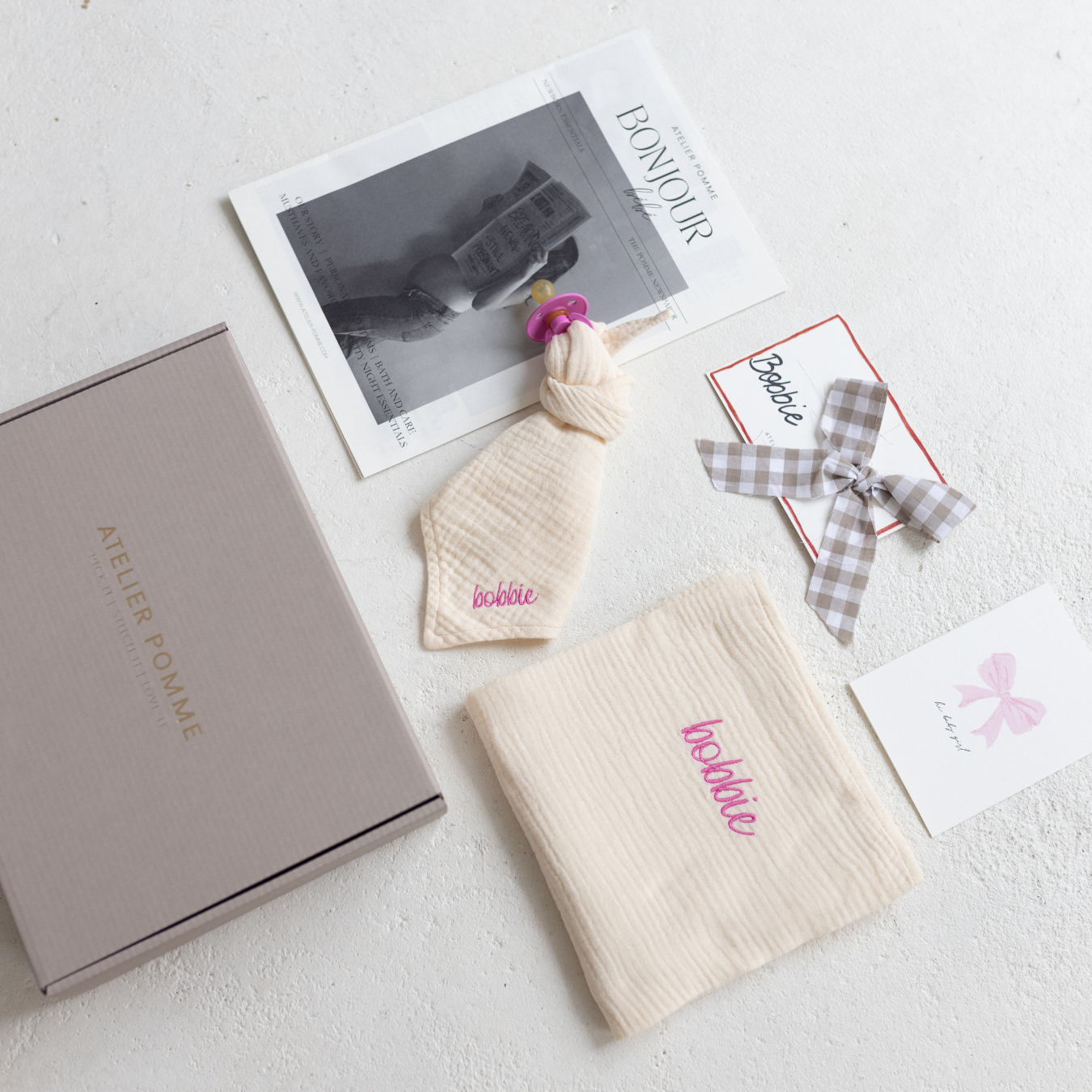 cadeaubox met magazine, naamkaartje, wenskaart, speen, speendoekje en laken met gepersonaliseerde tekst.
