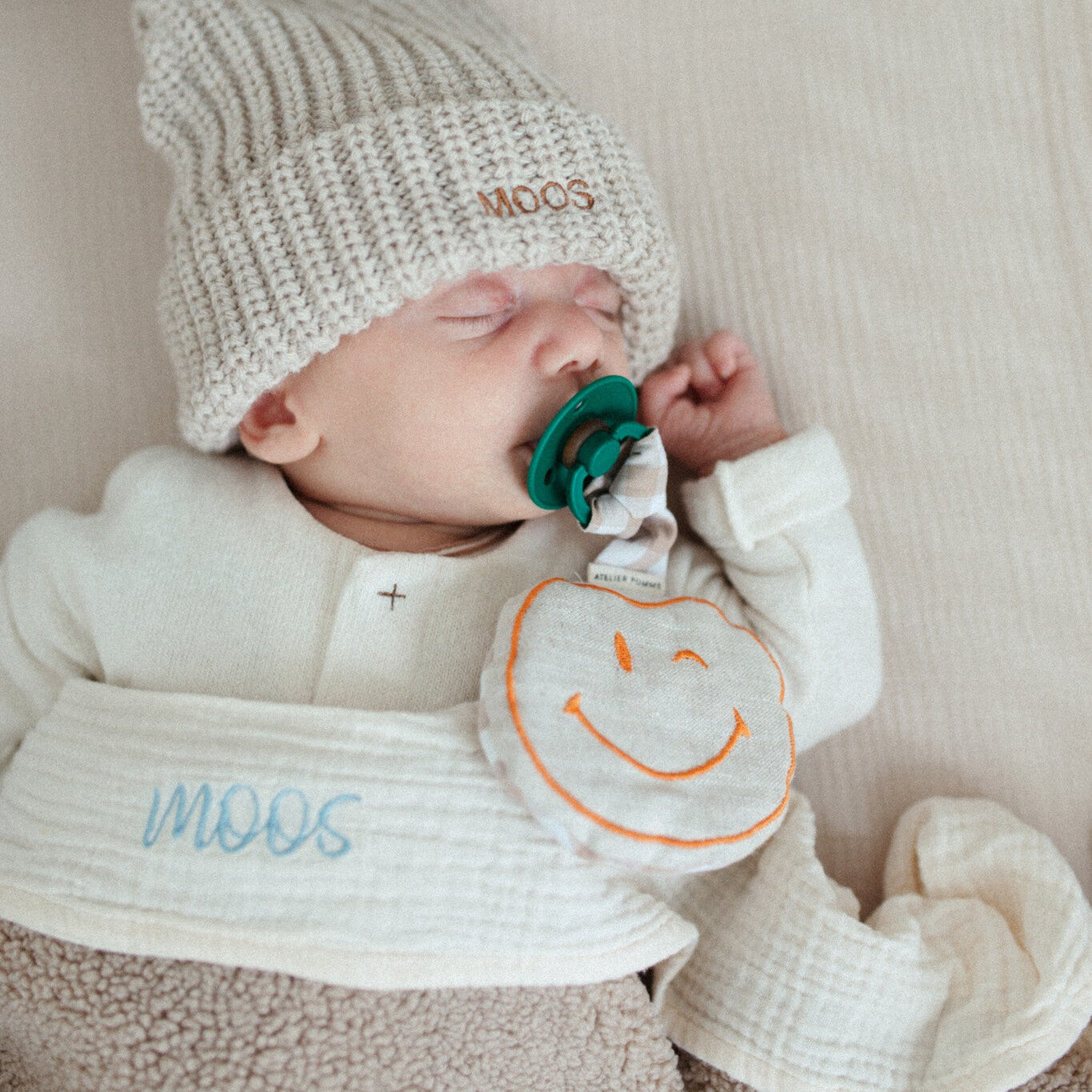 baby ligt onder laken met tekst. muts met tekst, speen met speenknuffel.
