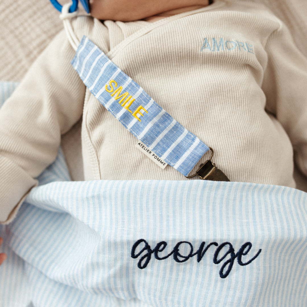 baby ligt onder laken met gepersonaliseerde tekst, speenkoord