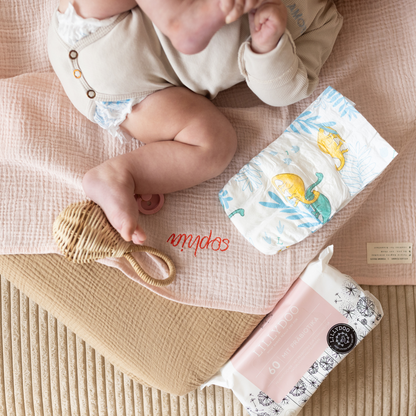 baby ligt op gepersonaliseerde laken met luier, babydoekjes, speen en rammelaar