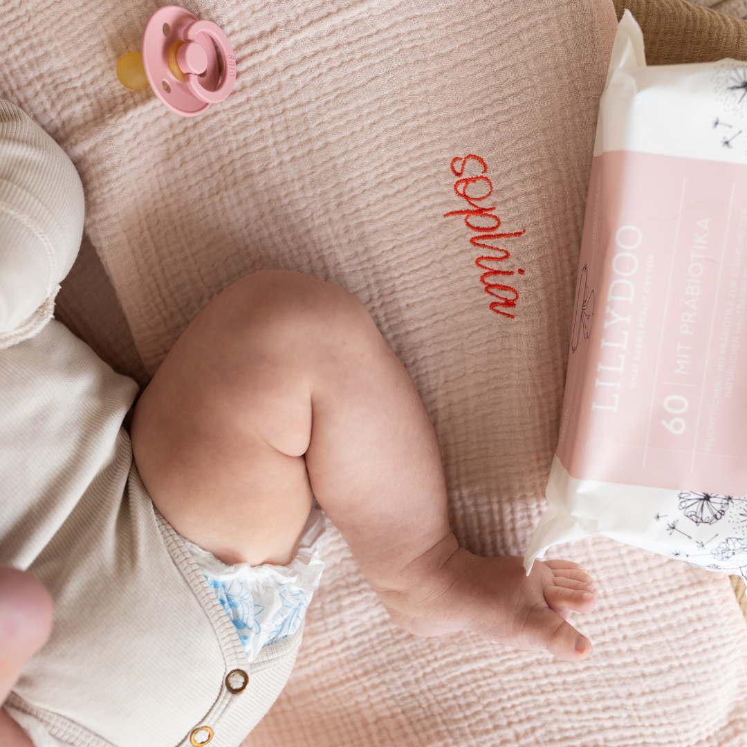 baby ligt op gepersonaliseerde laken met babydoekjes en speen 