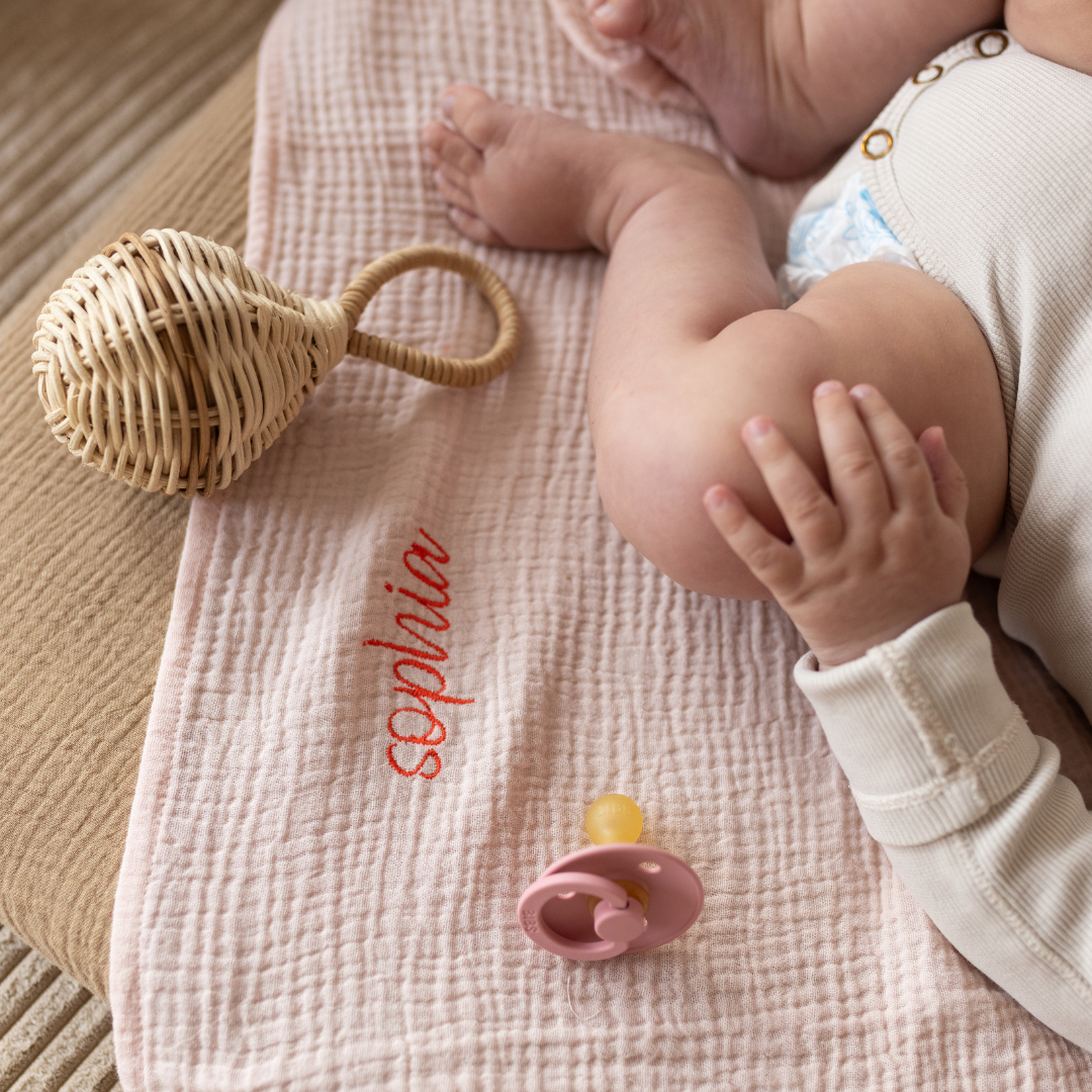 baby ligt op laken met gepersonaliseerde tekst, speen en rammelaar. 