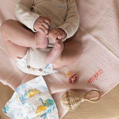 baby ligt op gepersonaliseerde laken met luier, speen en rammelaar 