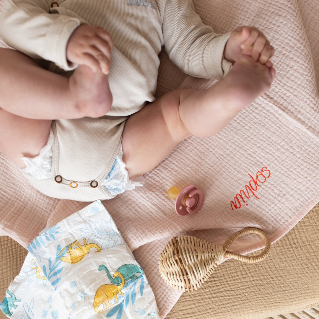 baby ligt op gepersonaliseerde laken met luier, speen en rammelaar 