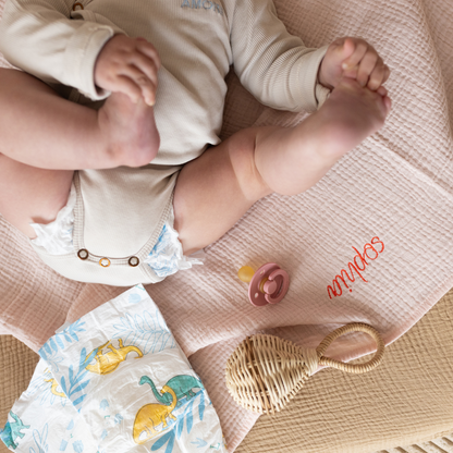 baby ligt op gepersonaliseerde laken met luier, speen en rammelaar 
