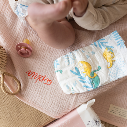 baby ligt op gepersonaliseerde laken met luier, speen en rammelaar 