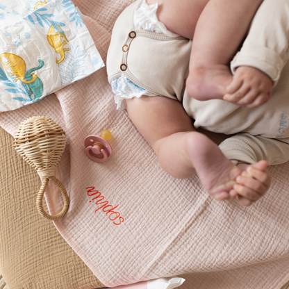 baby ligt op laken met luier, speen en rammelaar 