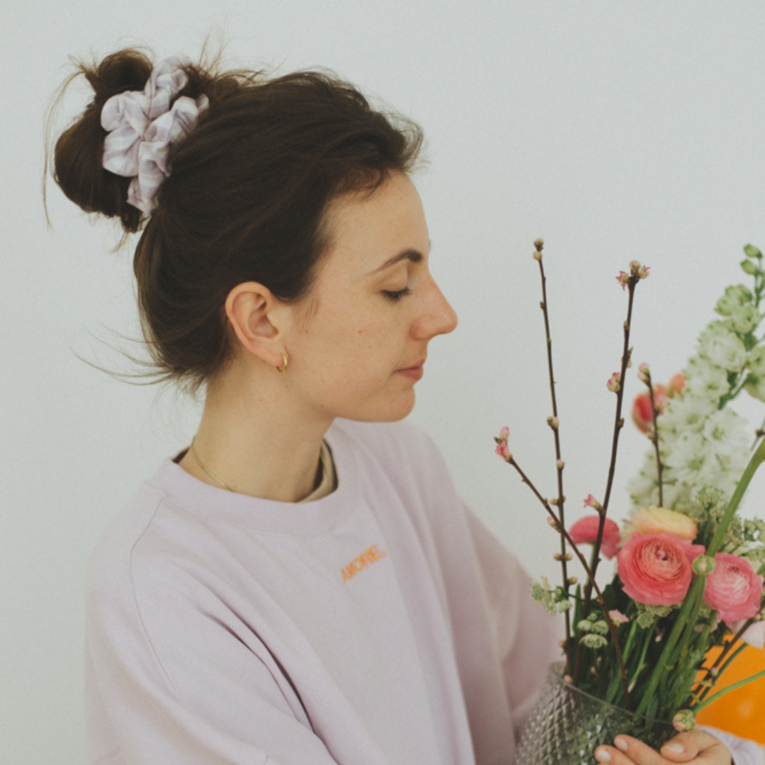 Een vrouw met een geblokte lila scrunchie in haar haar. De perfecte accessoires gecombineerd met een lila sweater. 